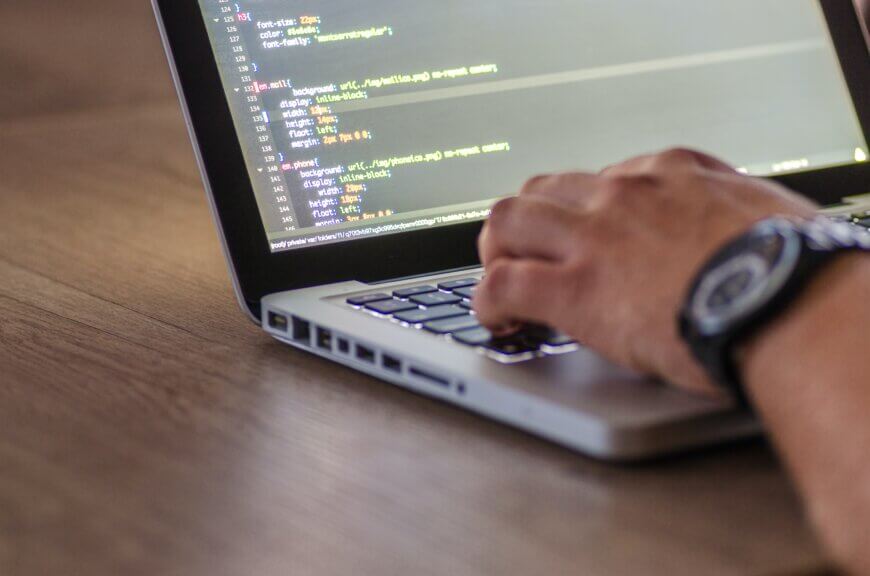 Side angle of man typing on laptop with his screen being code.