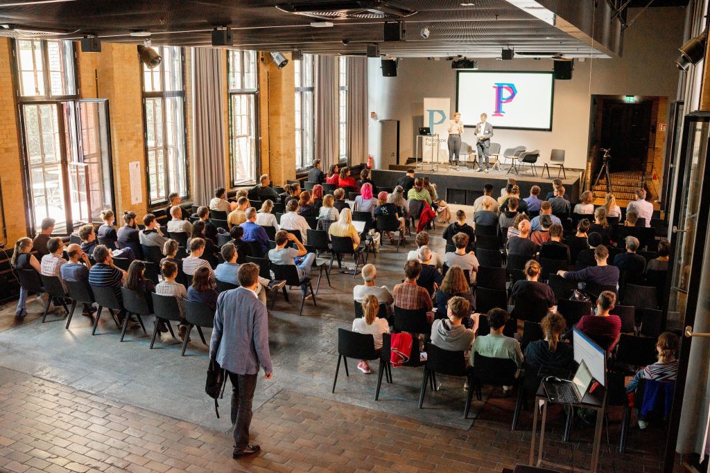 Picture showcasing one of the rooms at bUm in Berlin, Germany, the venue of the Nextcloud Community Conference 2025. It depicts a stage with two people, as well as an audience listening to the speakers.
